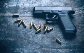 Hand Gun with Ammunition on Dark background. 9 mm Pistol Military Weapon and Pile of Bullets Ammo at the Metal Table For Demonstrations. PHOTO/ Courtesy