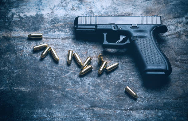 Hand Gun with Ammunition on Dark background. 9 mm Pistol Military Weapon and Pile of Bullets Ammo at the Metal Table For Demonstrations. PHOTO/ Courtesy
