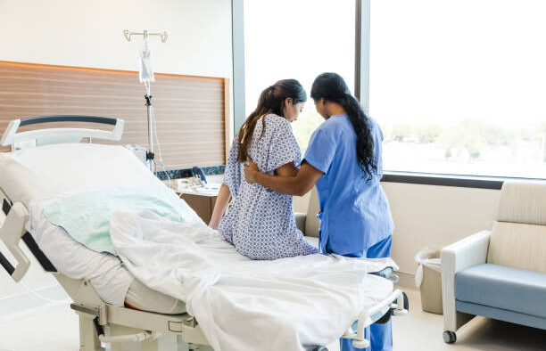 An Unrecognizable Female Nurse Helps the Unrecognizable Woman Get out of the Hospital Bed. PHOTO/ Courtesy