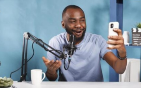image of a creator recording a podcast using a phone and a desktop microphone setup. PHOTO/ Vecteezy